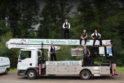 Das Team der Zimmerei Wolf verteilt auf dem eigenen Kranwagen, dessen Ausleger die Aufschrift „Zimmerei & Holzbau Wolf“ trägt und auf dessen Aufbau „Wir leben Holz“ steht.