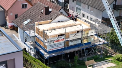 Luftaufnahme einer Aufstockung in Holzrahmenbauweise: auf einem bestehenden Haus steht die neue Holzkonstruktion mit offener Deckenlage, ringsum ein Gerüst.