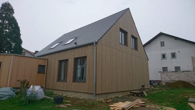 Neubau mit senkrechter Holzschalung aus hellem Nadelholz, dunkel gedecktem Satteldach und zwei Dachflächenfenstern.