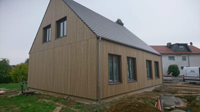 Giebelseite desselben Neubaus: die senkrechte Holzschalung läuft ohne Absatz über zwei Geschosse, das Dach ist mit dunklen Ziegeln gedeckt.