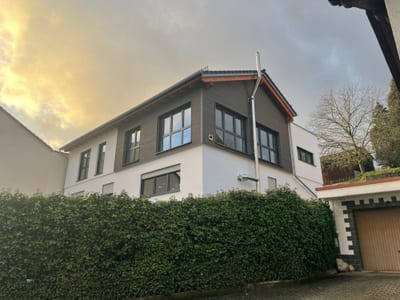 Aufgestocktes Wohnhaus im Abendlicht: das neue Obergeschoss ist mit dunkler Holzschalung verkleidet und schließt mit einem flach geneigten Dach ab.