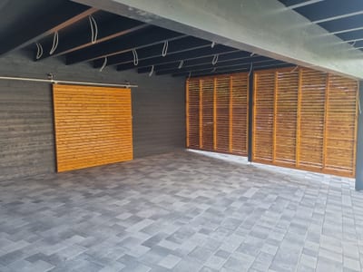 Innenansicht des Carports: ein Schiebetor aus Holzlatten läuft an einer Schiene, seitlich schließt eine Lamellenwand den Stellplatz ab.
